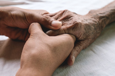 Hands of the old man and a young man on a white bed in a hospital